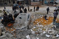 Pessoas apanham laranjas nos escombros de um mercado atingido  por um ataque aéreo na cidade rebelde de Maarrat Misrin, na Síria. 