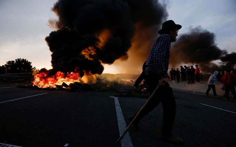 Um homem passa em frente a um fogo onde os agricultores espanhóis bloquearam a autoestrada AP-7, perto de Girona. Muitos protestos no país não foram, na sua maioria, comunicados às autoridades e aconteceram à margem da organização das grandes confederações agrícolas de Espanha.