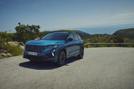 Carro azul viaja por estrada costeira com vista para o mar