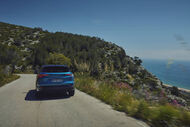 Um carro azul viaja numa estrada costeira