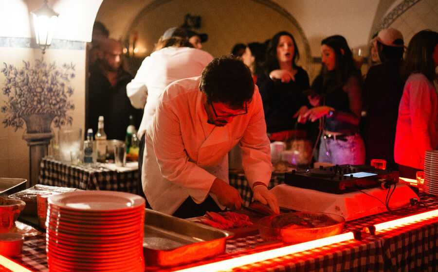 Um chef corta carne numa mesa durante um evento com várias pessoas