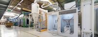 Equipamento industrial branco numa fábrica com trabalhadores ao fundo