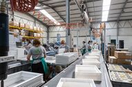 Funcionários trabalham na linha de produção, com equipamentos e produtos brancos