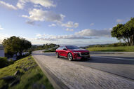 Um carro Mazda 6e vermelho numa estrada sinuosa com árvores e um céu azul