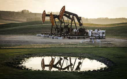 Reflexo de máquinas de extração de petróleo em charco perto de campo verdejante