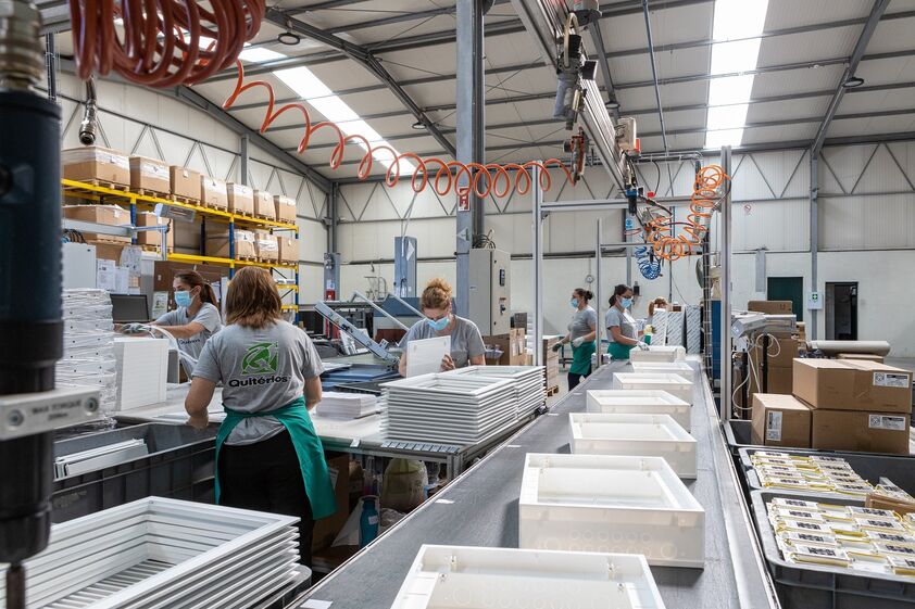 Funcionários trabalham na linha de produção, com equipamentos e produtos brancos