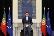 Ministro português discursa com as bandeiras de Portugal e da União Europeia
