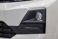 Detalhe da frente de um veículo branco, com foco na grelha e no farol
