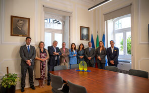 Grupo de pessoas posa para foto numa sala com bandeiras de Portugal