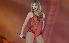 Taylor Swift atua num concerto com um body laranja brilhante e um microfone