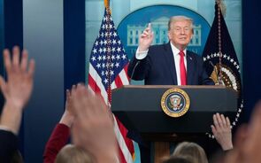 Donald Trump discursa com bandeiras dos EUA ao fundo numa conferência