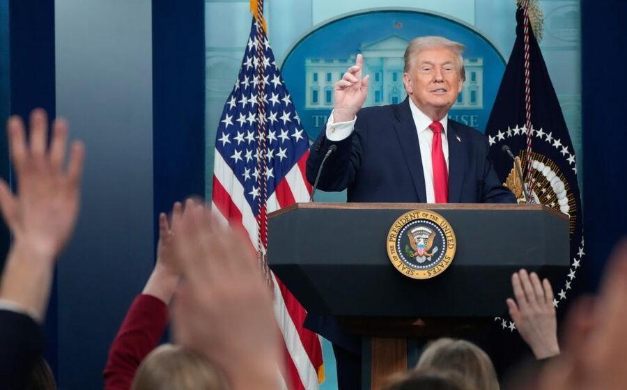 Donald Trump discursa com bandeiras dos EUA ao fundo numa conferência