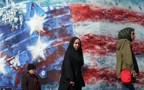 Iranianos em frente a um cartaz anti-EUA no Irão