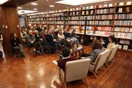 Pessoas assistem a evento numa livraria com estantes cheias de livros