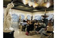 Pessoas assistem a palestra num museu com estátuas e azulejos
