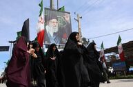Mulheres iranianas passam perto de um cartaz do antigo líder supremo, quando se encaminham para um funeral.