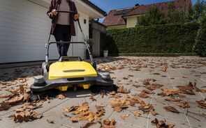 Mulher usa máquina de varrer folhas no jardim de uma casa