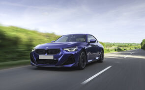 Um BMW azul anda numa estrada ladeada por vegetação