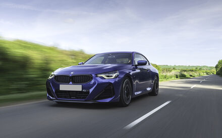 Um BMW azul anda numa estrada ladeada por vegetação