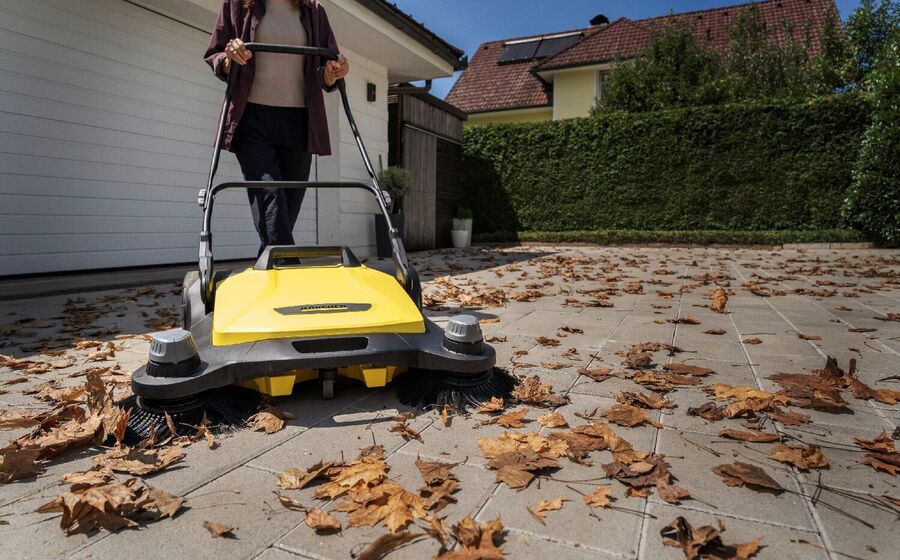 Mulher usa máquina de varrer folhas no jardim de uma casa