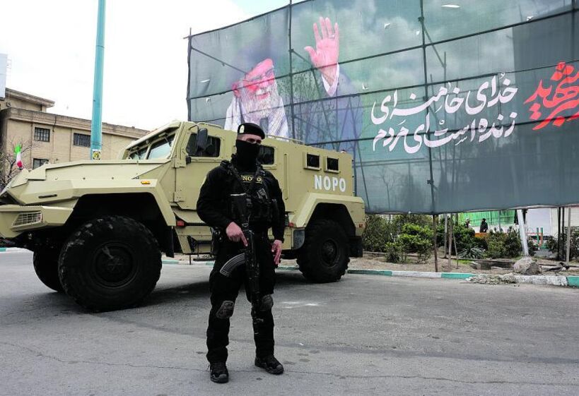 membros das forças de segurança iraniana junto a cartaz a homenagear o falecido líder supremo do Irão.