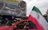 Homem faz o sinal de vitória enquanto passa em frentea um cartaz, em teerão, que mostra aviões americanos a cair em redes iranianas.