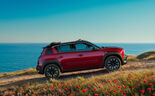 Automóvel vermelho numa colina com vista para o oceano e um campo de papoilas