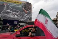 Homem faz o sinal de vitória enquanto passa em frentea um cartaz, em teerão, que mostra aviões americanos a cair em redes iranianas.