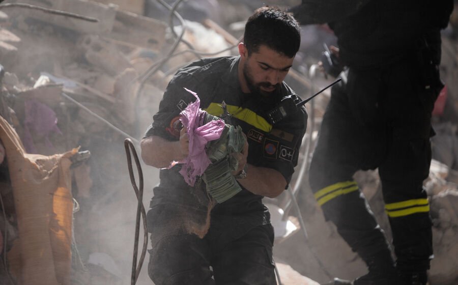 Um elemento das equipas de resgate retira dinheiro dos destroços de um edifício em Beirute atingido pela ofensiva israelita.