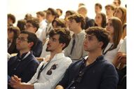 Pessoas assistem a evento em espaço fechado com atenção