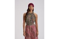 Mulher posa com vestido comprido e padrão paisley, e usa um gorro vermelho