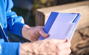 Homem lê correspondência com envelope azul e conteúdo branco